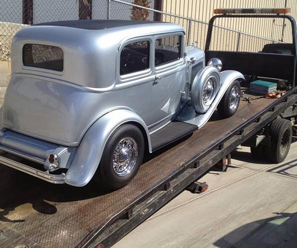 old school silver car on a tow truck flat bed